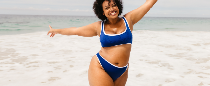 plus sized woman in a blue bikini at the beach showing off her weight loss from weight loss medication.