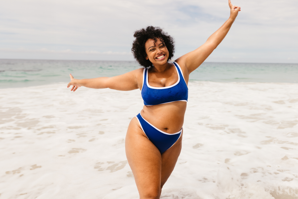 plus sized woman in a blue bikini at the beach showing off her weight loss from weight loss medication.