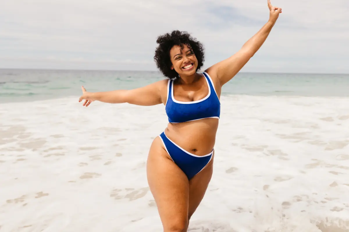plus sized woman in a blue bikini at the beach showing off her weight loss from weight loss medication.